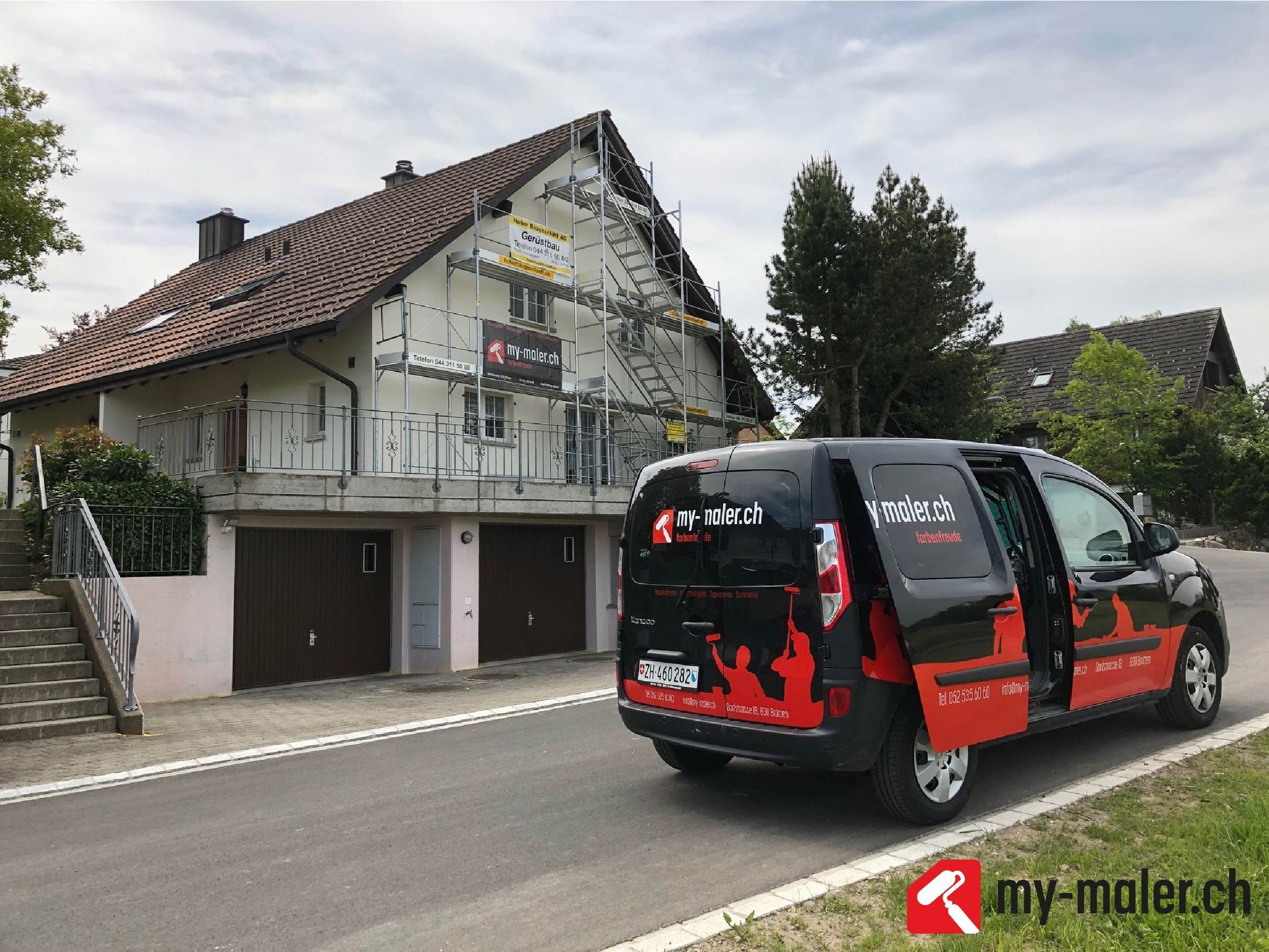 Ein schwarz - roter Lieferwagen steht vor einem Haus.