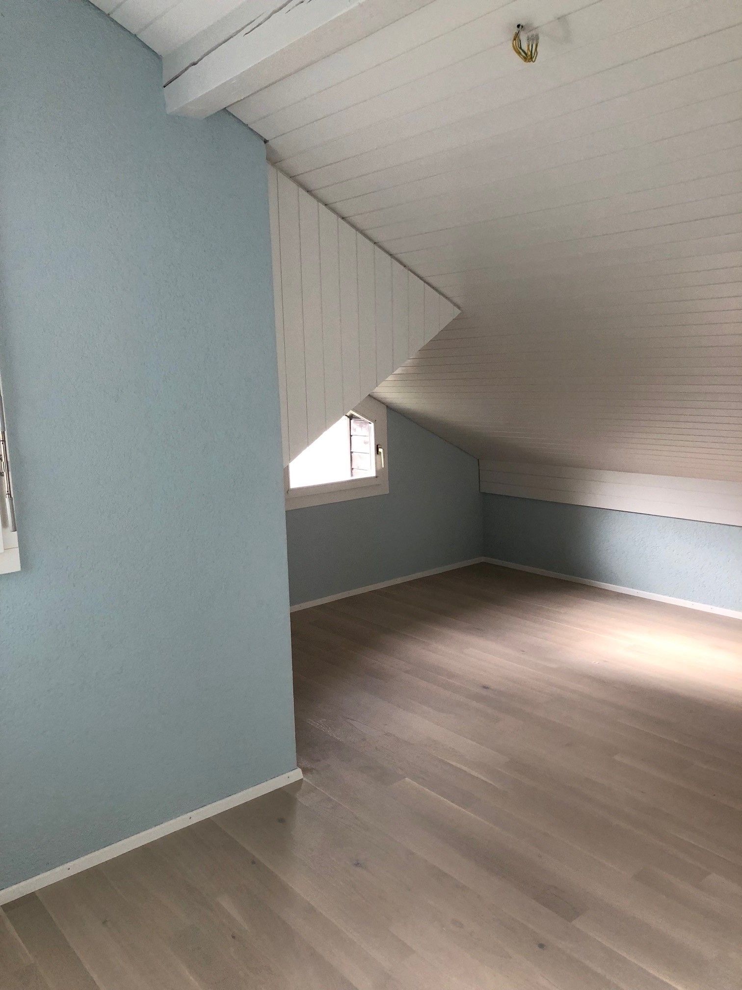 Ein leerer Dachboden mit blauen Wänden und einer weissen Decke.