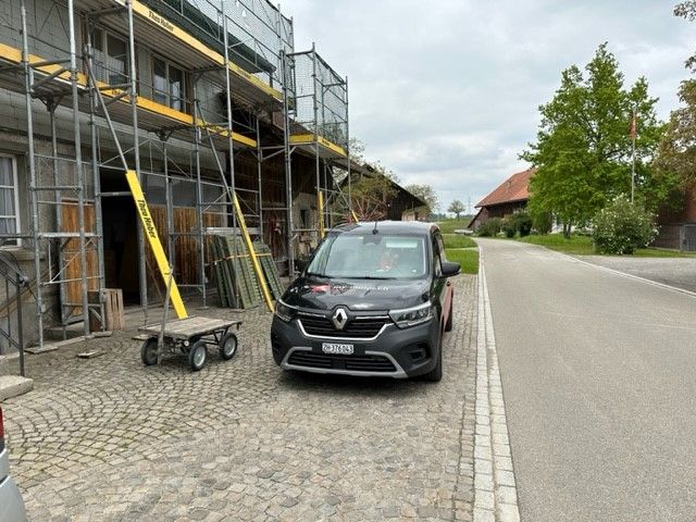 Ein schwarzer Lieferwagen parkt vor einem im Bau befindlichen Gebäude.