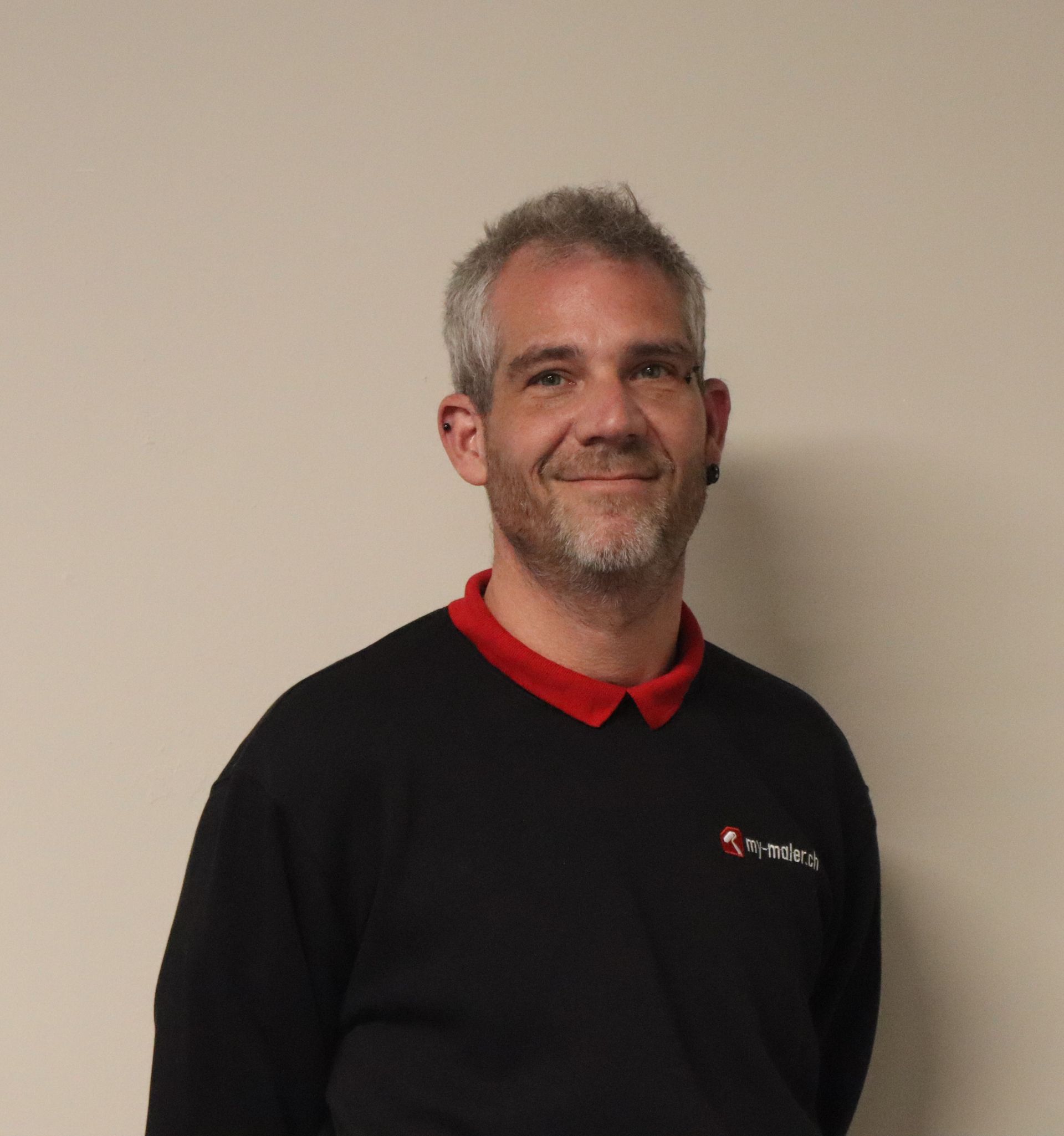 Eine Frau in einem schwarz-roten Poloshirt lächelt vor einem Baum.