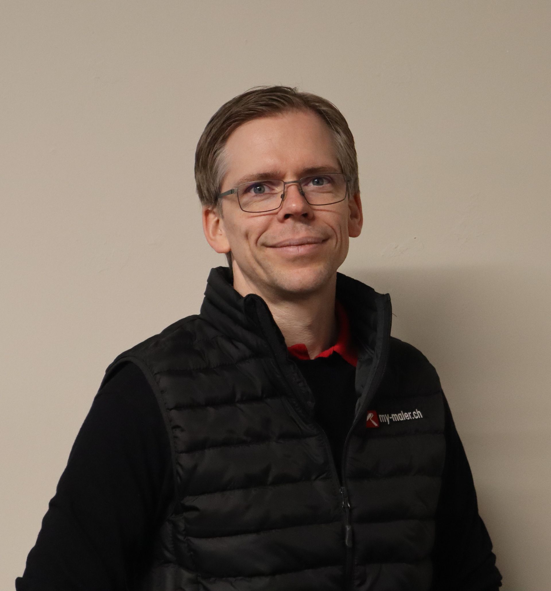 Ein Mann in einem schwarz - roten Poloshirt lächelt in die Kamera.