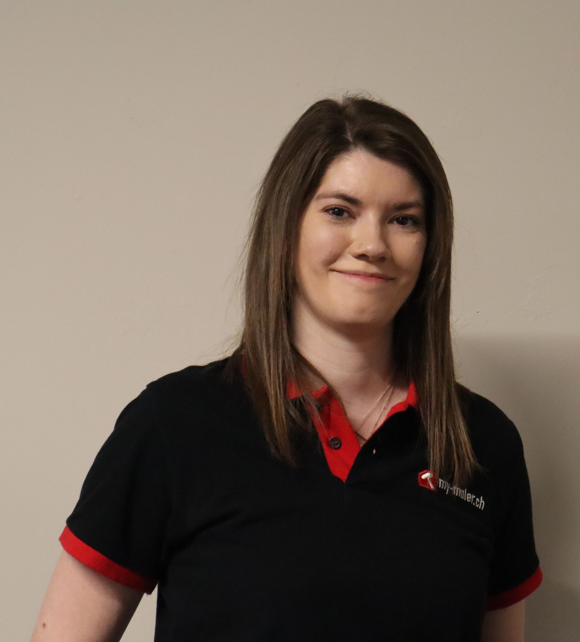 Eine junge Frau in einem schwarz-roten Poloshirt lächelt in die Kamera.