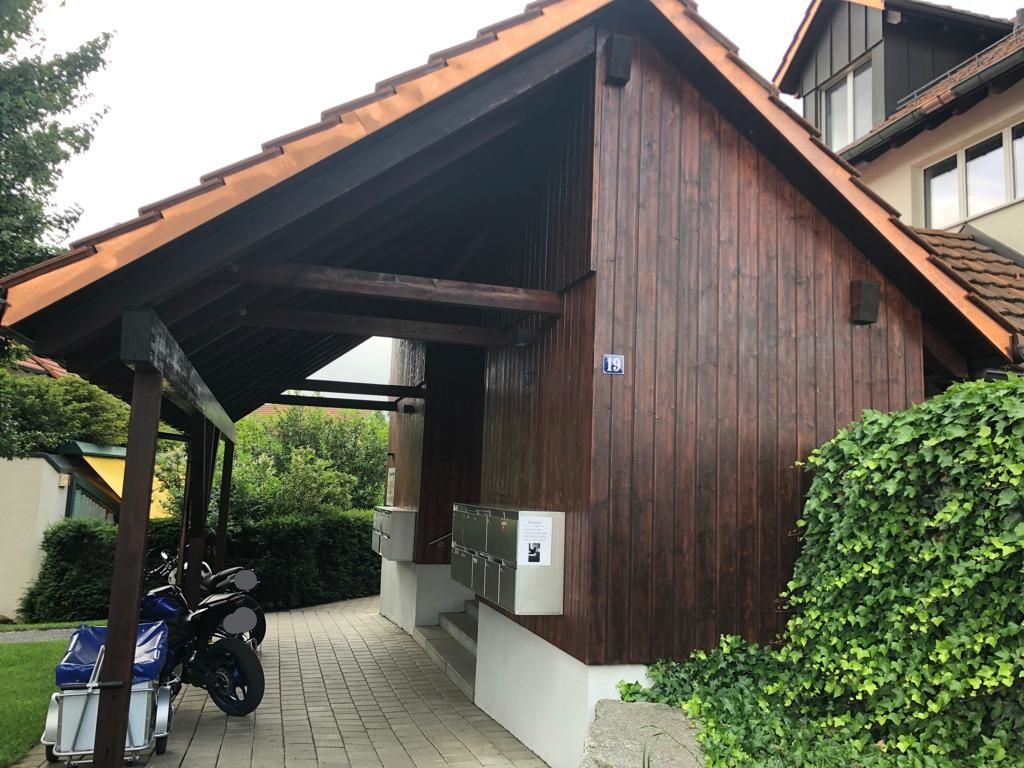 Ein Motorrad ist unter einem Holzschuppen vor einem Haus geparkt.