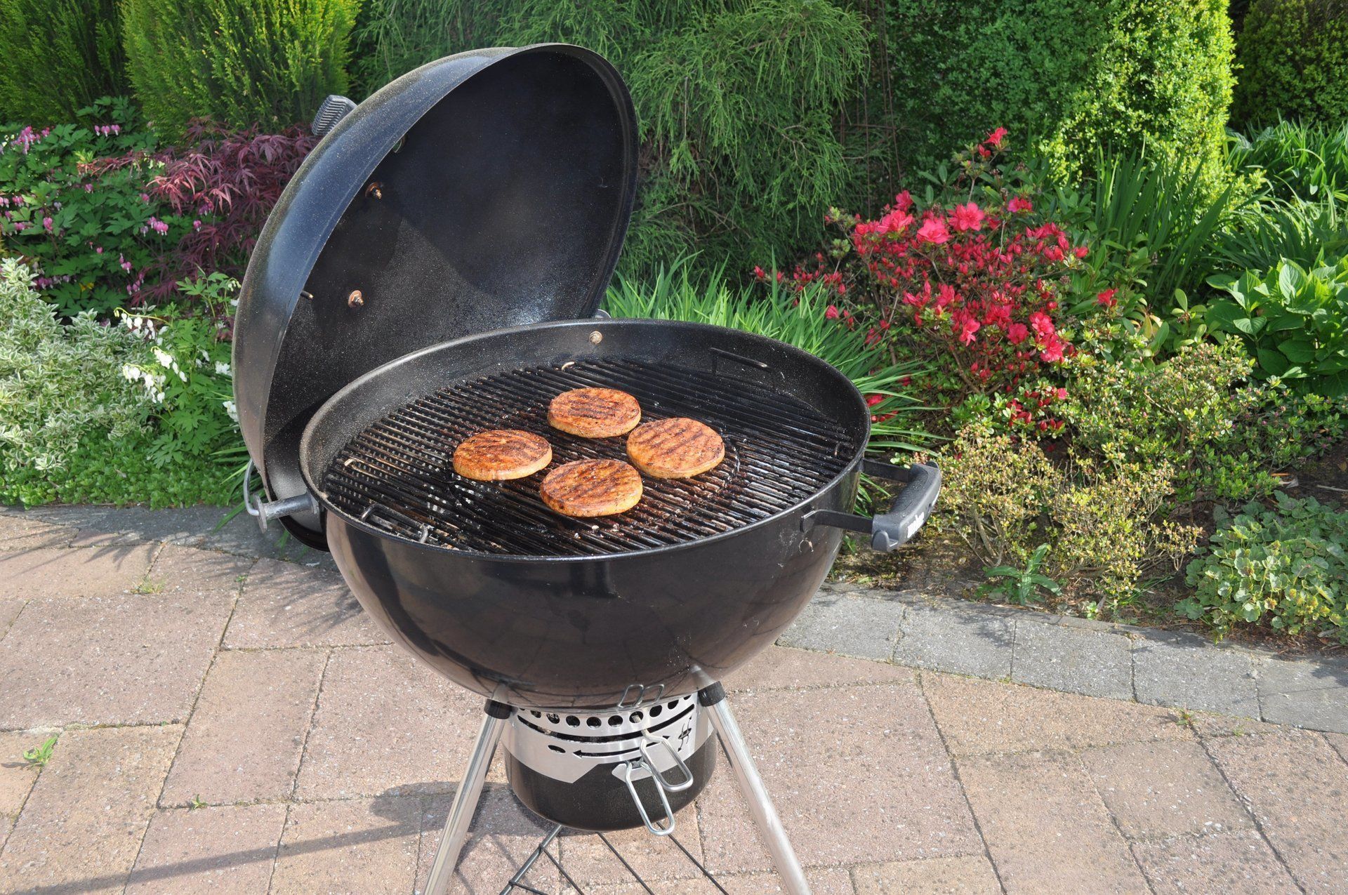 Zwarte houtskoolgrill met hamburgers die buiten worden bereid. Deksel gedeeltelijk open.