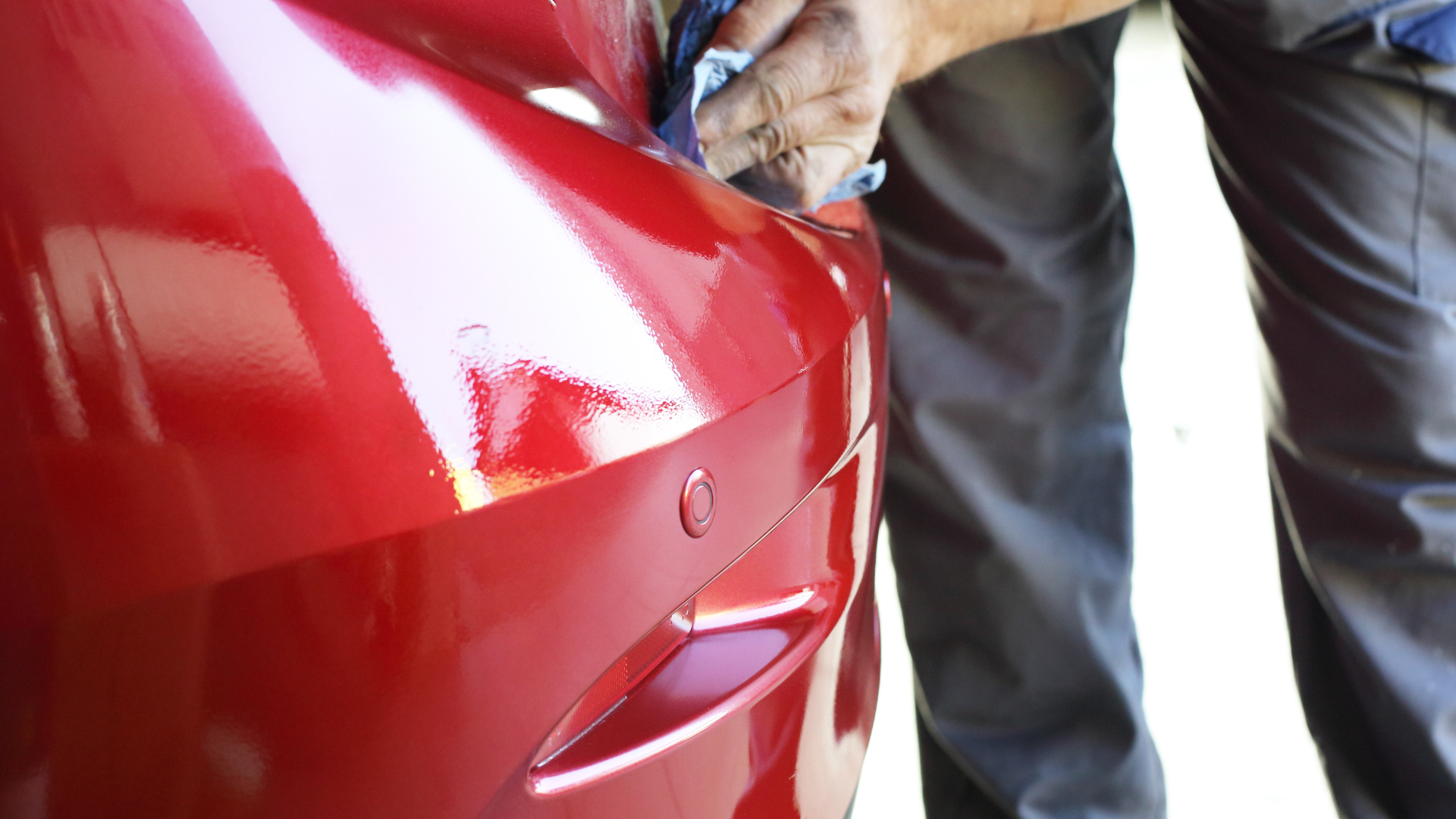 Person wiping a shiny red car bumper.