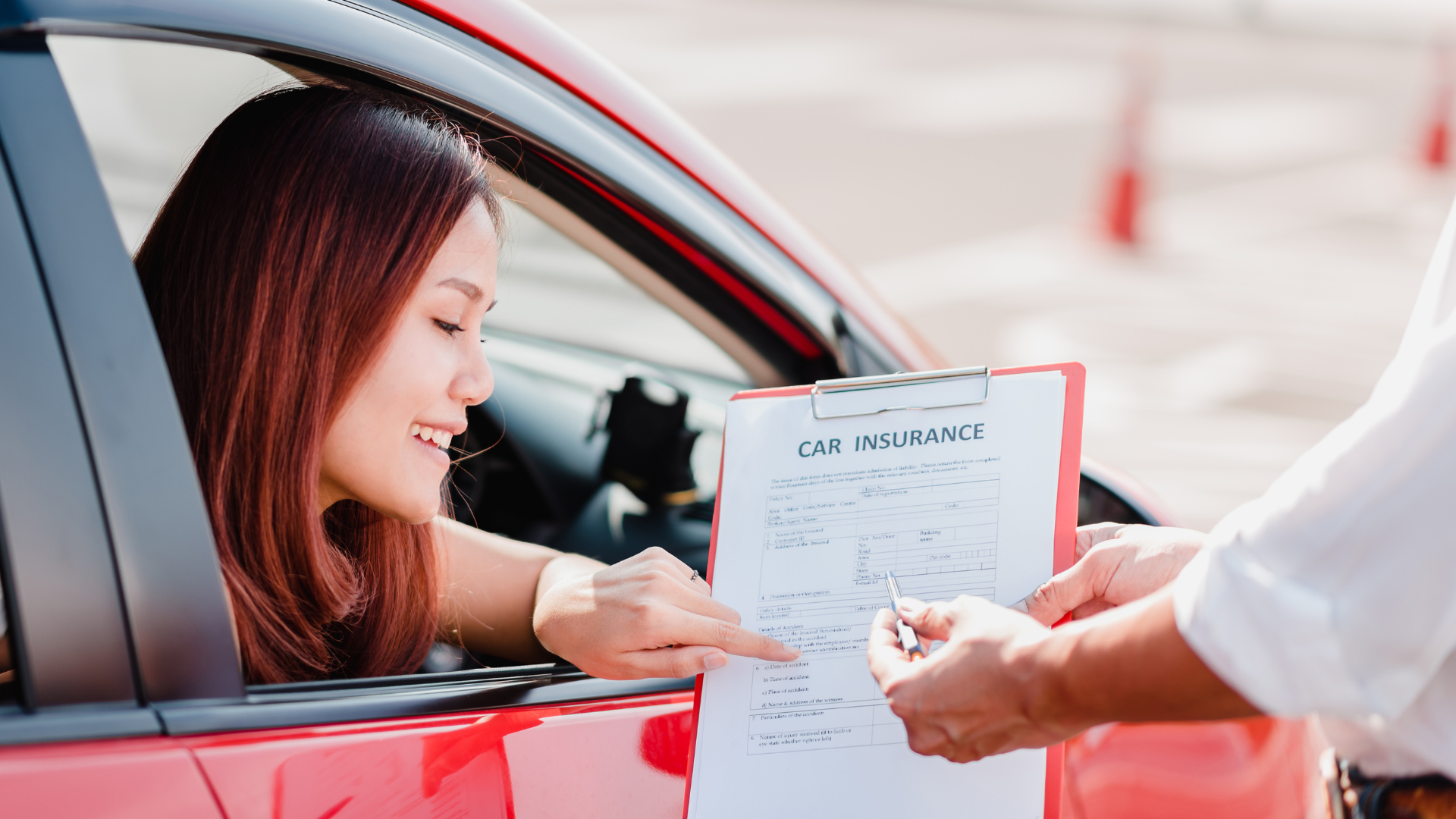 Woman in red car reviewing car insurance document with an agent, outdoors.