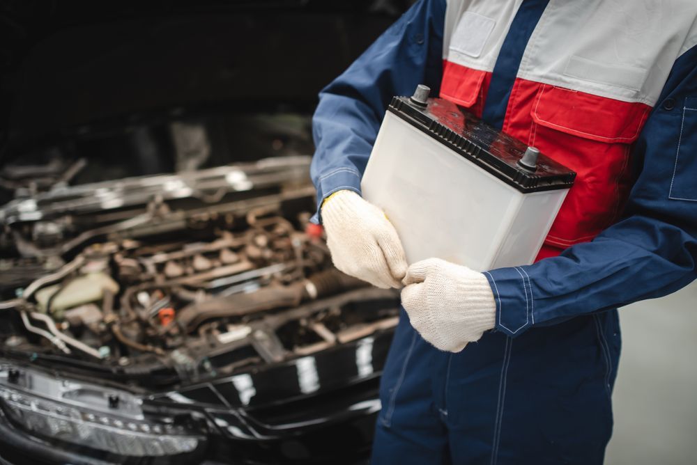 A Mechanic Is Holding A Battery In Front Of A Car — Advanced Windscreens & Service Centre In Proserpine, QLD