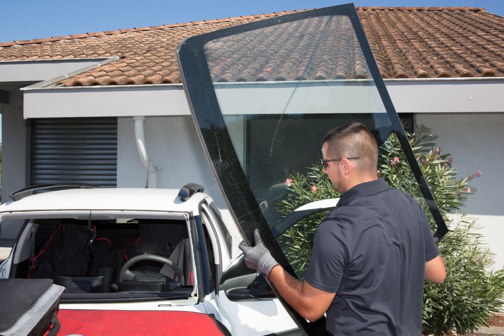 A Man Is Installing A Windshield On A Car In Front Of A House — Advanced Windscreens & Service Centre In Proserpine, QLD