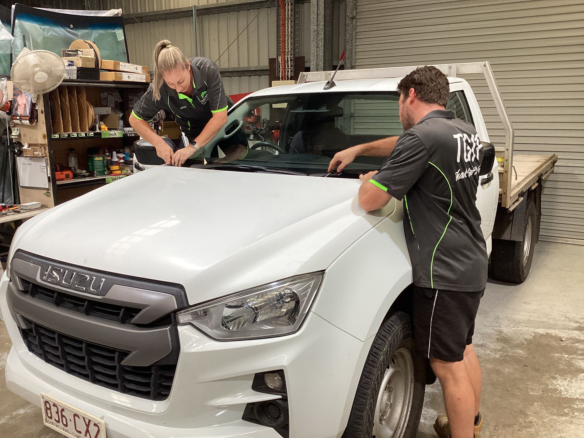 A Woman And A Man Are Replacing A Windscreen On A Car  In A Garage — Advanced Windscreens & Service Centre In Proserpine, QLD