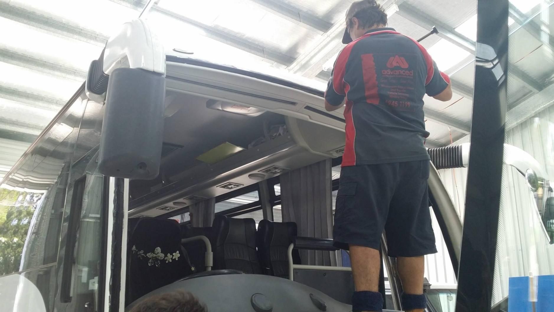 A Man Is Working On The Roof Of A Bus In A Garage — Advanced Windscreens & Service Centre In Cannonvale, QLD
