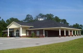 A single-story brick building with a dark roof and a covered entryway supported by white columns under a clear blue sky.