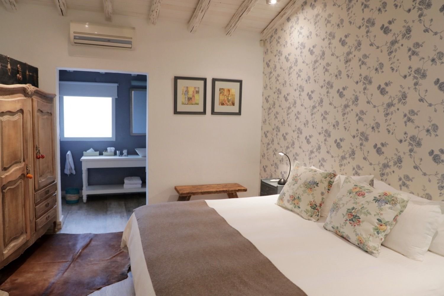 Bedroom with floral wallpaper, a large wooden armoire, and an en-suite bathroom visible.
