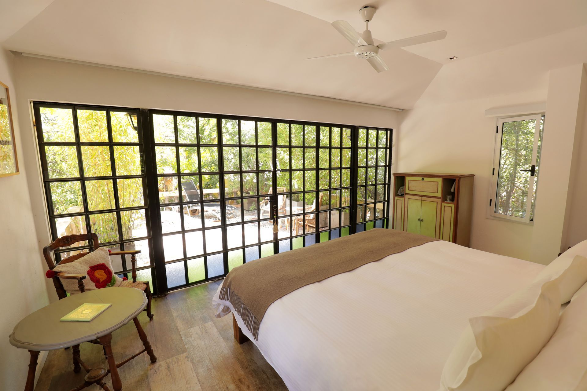 Bedroom with a bed facing a large glass door and a small window. The door overlooks a green outdoor area.