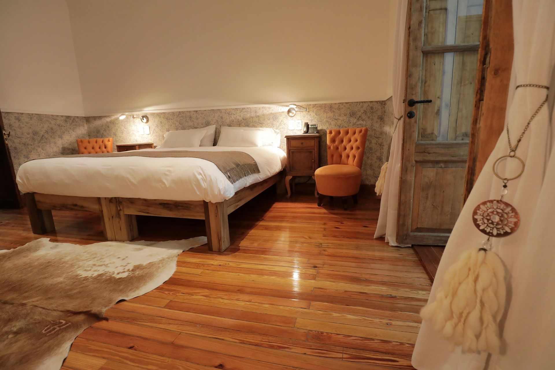 Bedroom with a large bed, wooden floor, patterned wallpaper, armchair, and a door to an outdoor space.
