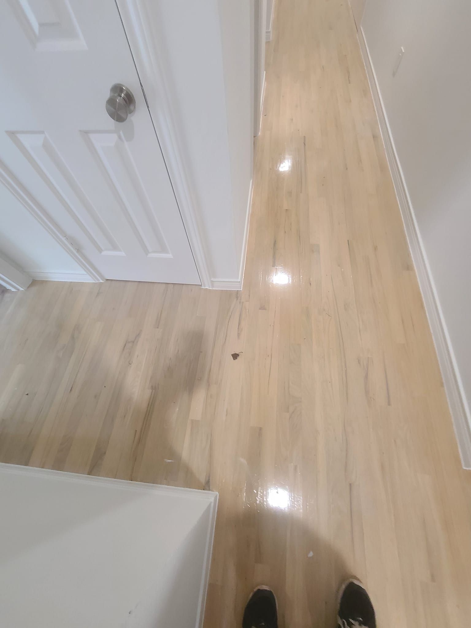 A person is standing on a wooden floor in a hallway.