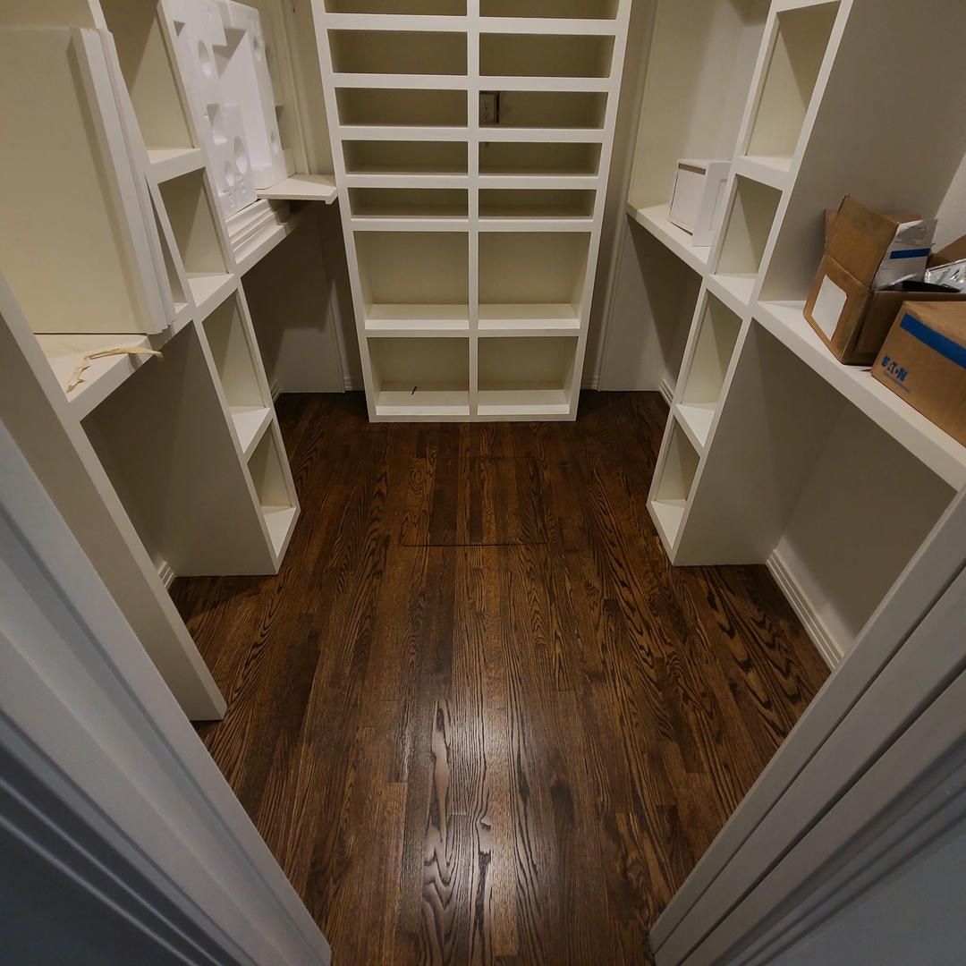 A walk in closet with wooden floors and white shelves