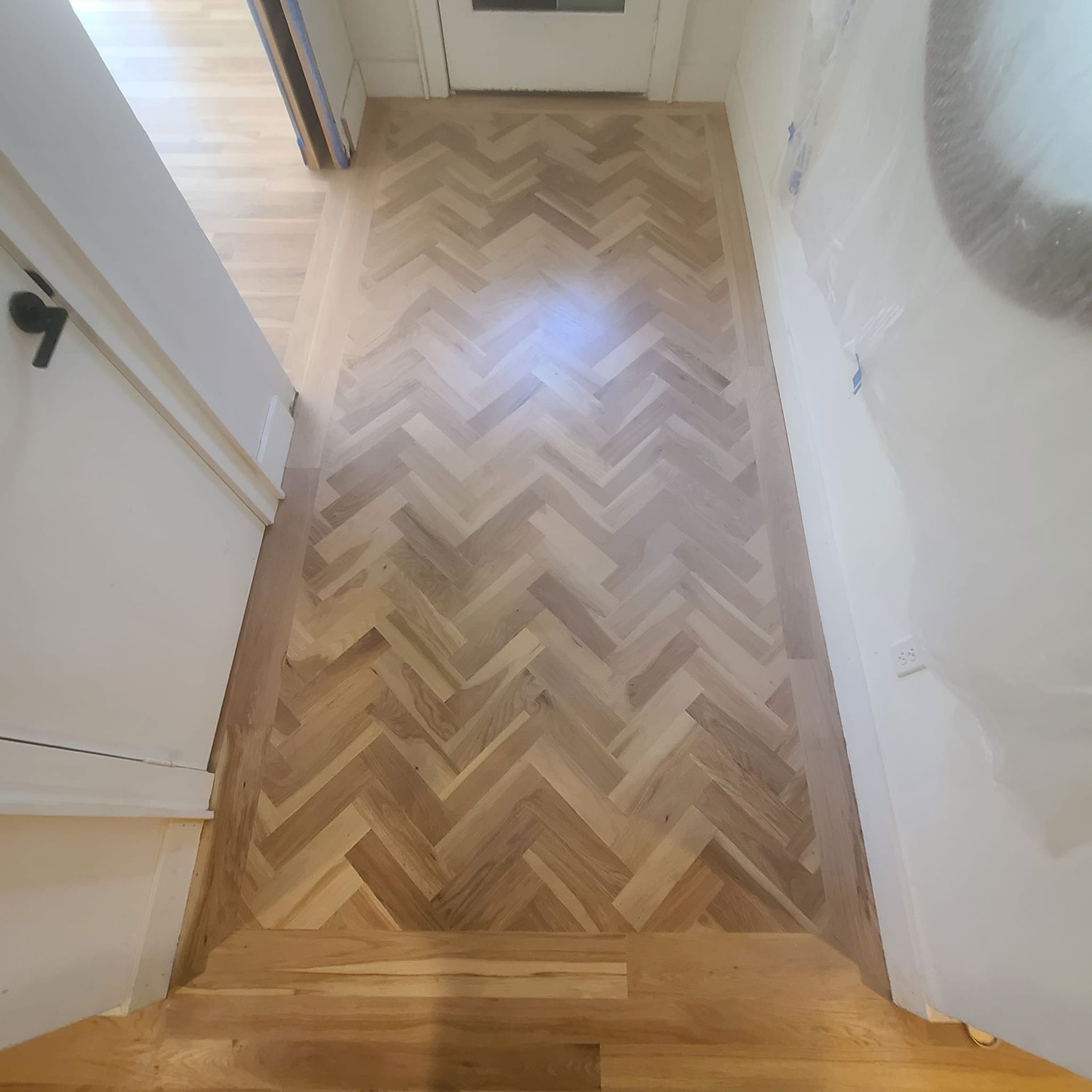 A wooden floor with a herringbone pattern in a hallway.