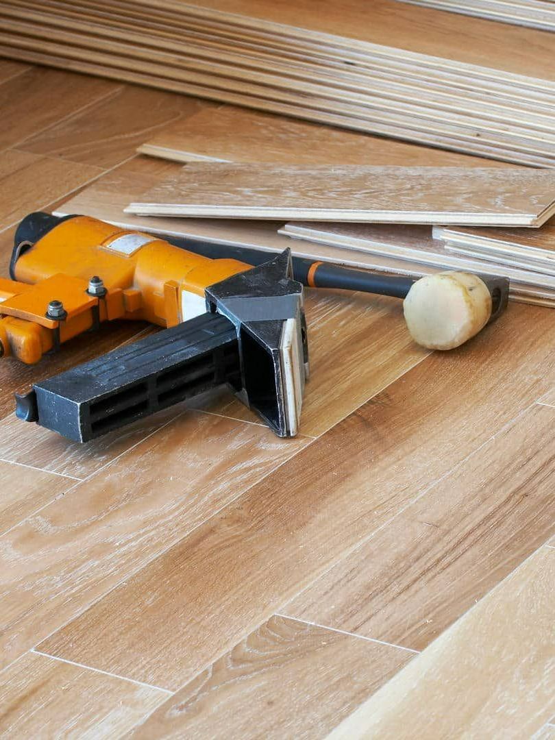 Flooring installation: Nail gun and mallet on laminate flooring, with stacks of planks in the background.