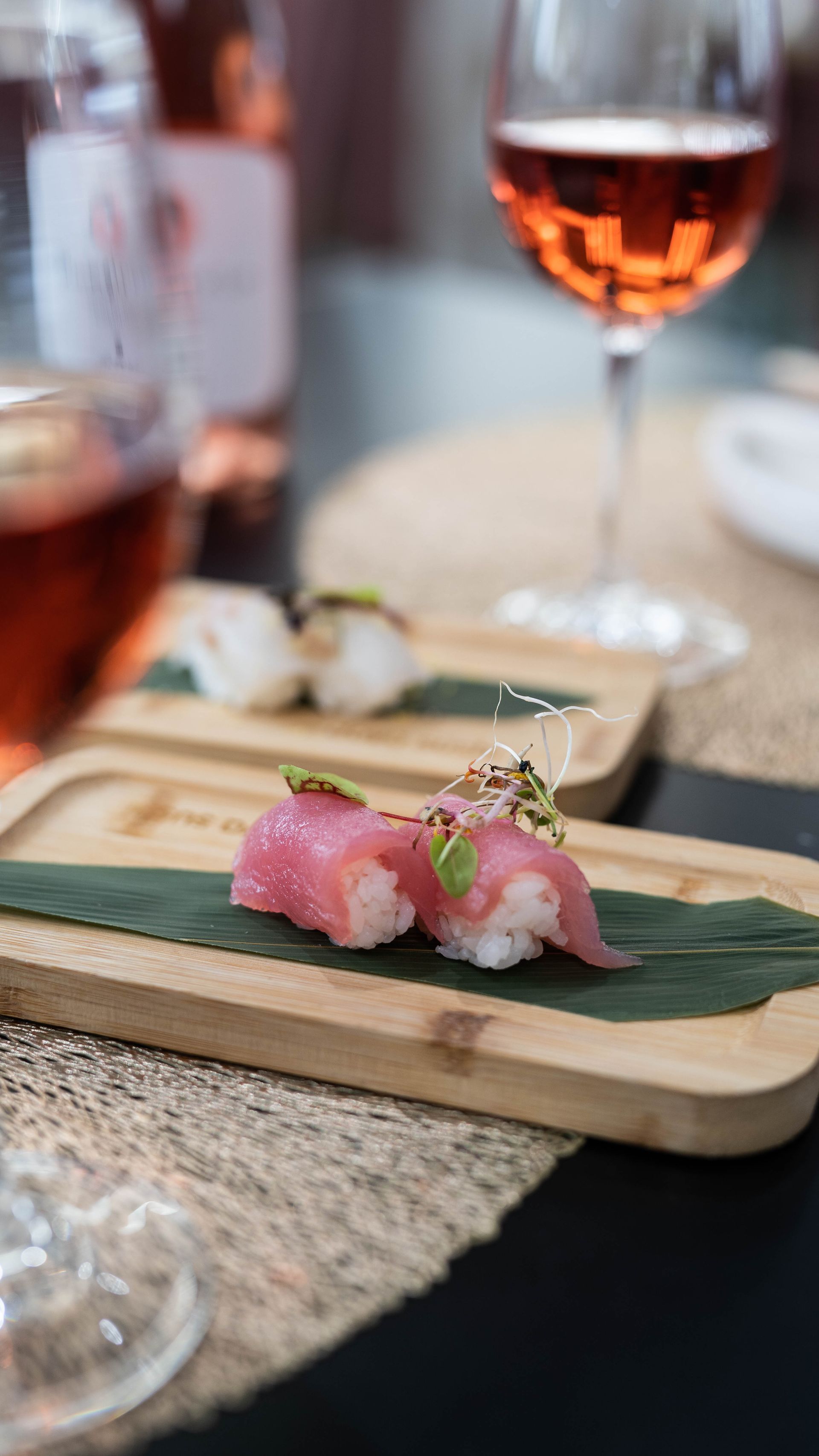 Un primo piano di sushi su un vassoio di legno con un bicchiere di vino in sottofondo.