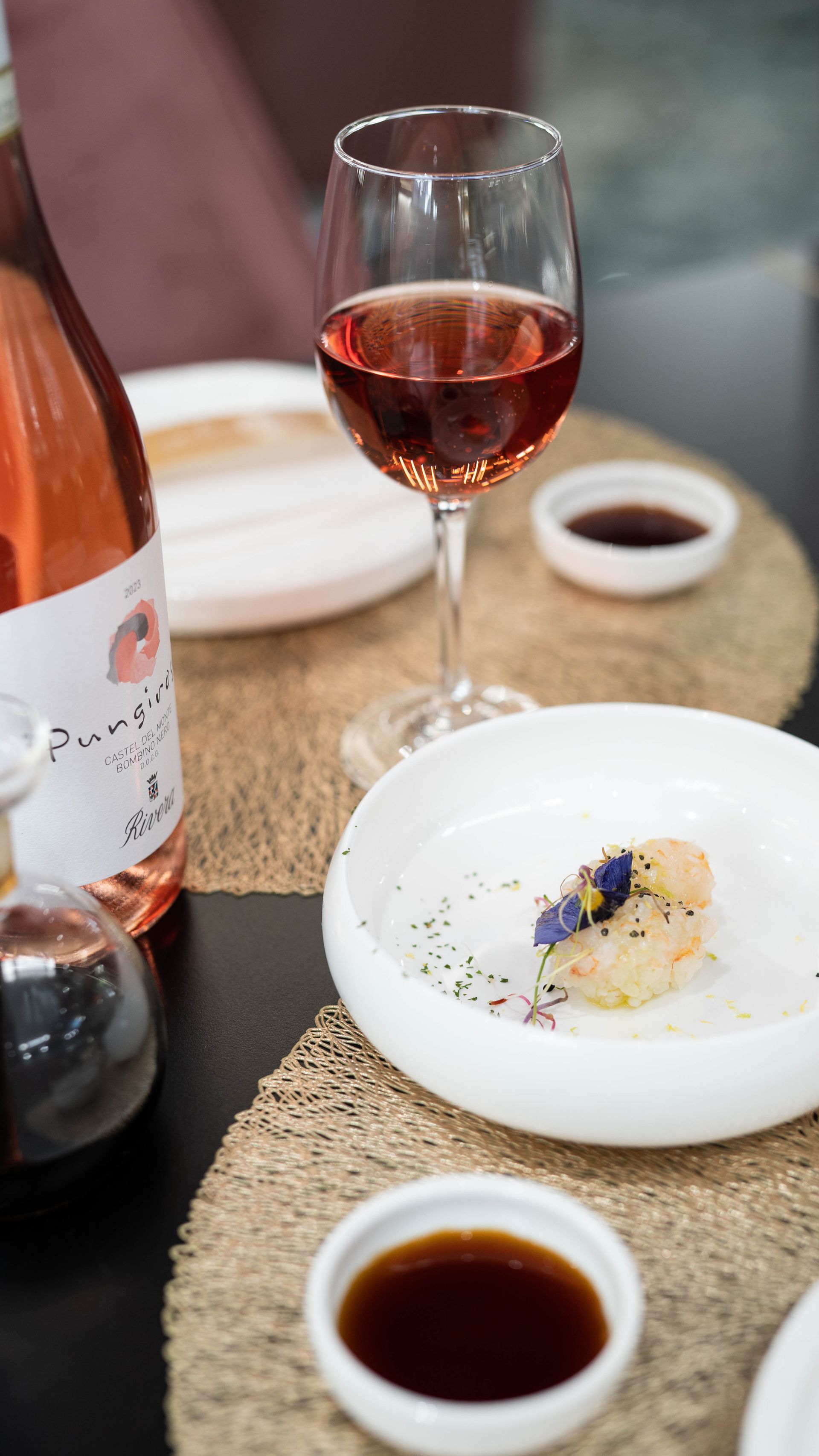 Una bottiglia di vino e un bicchiere di vino sono su un tavolo accanto a un piatto di cibo.