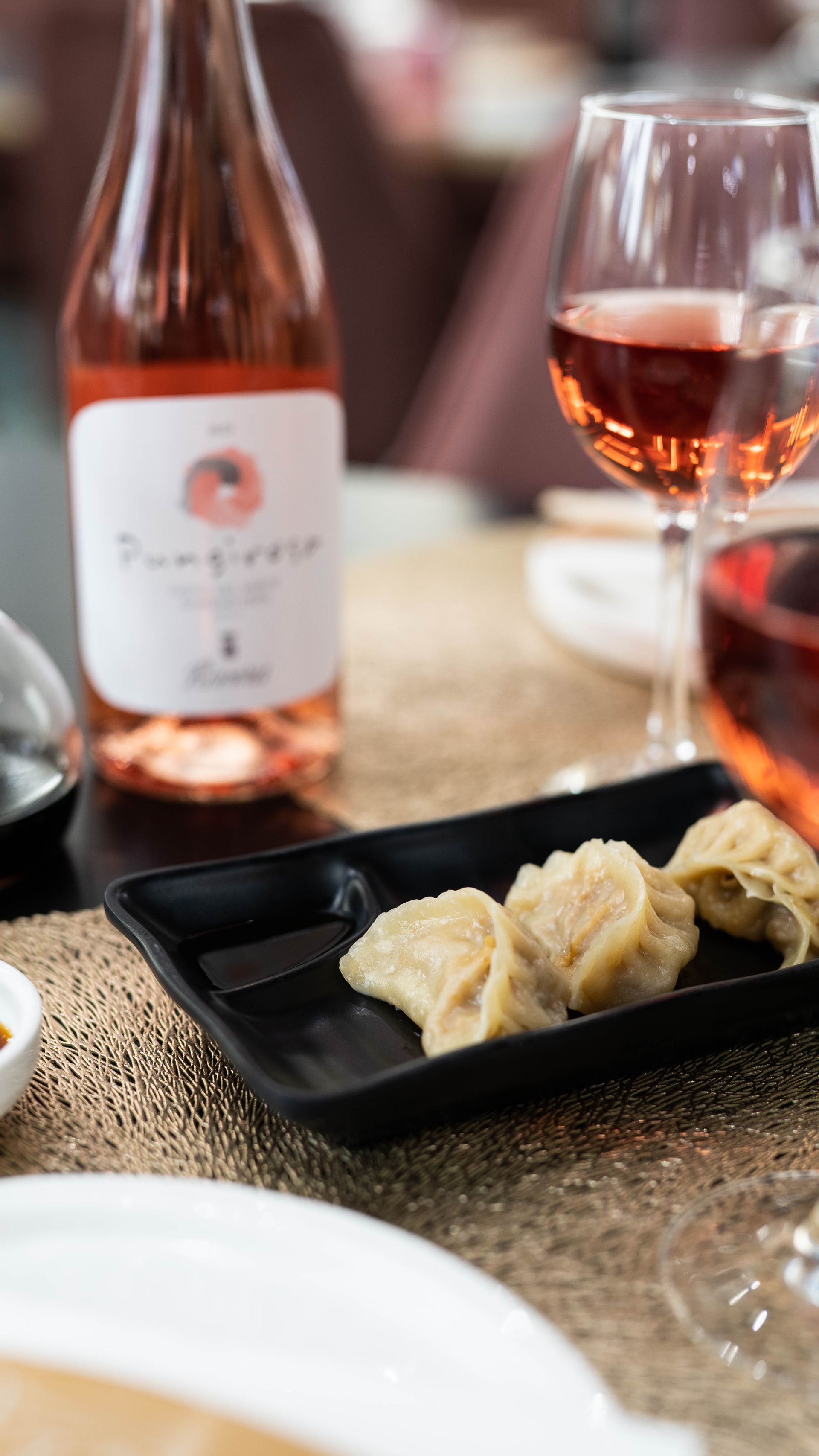 Una bottiglia di vino e un bicchiere di vino sono su un tavolo accanto a un piatto di gnocchi.