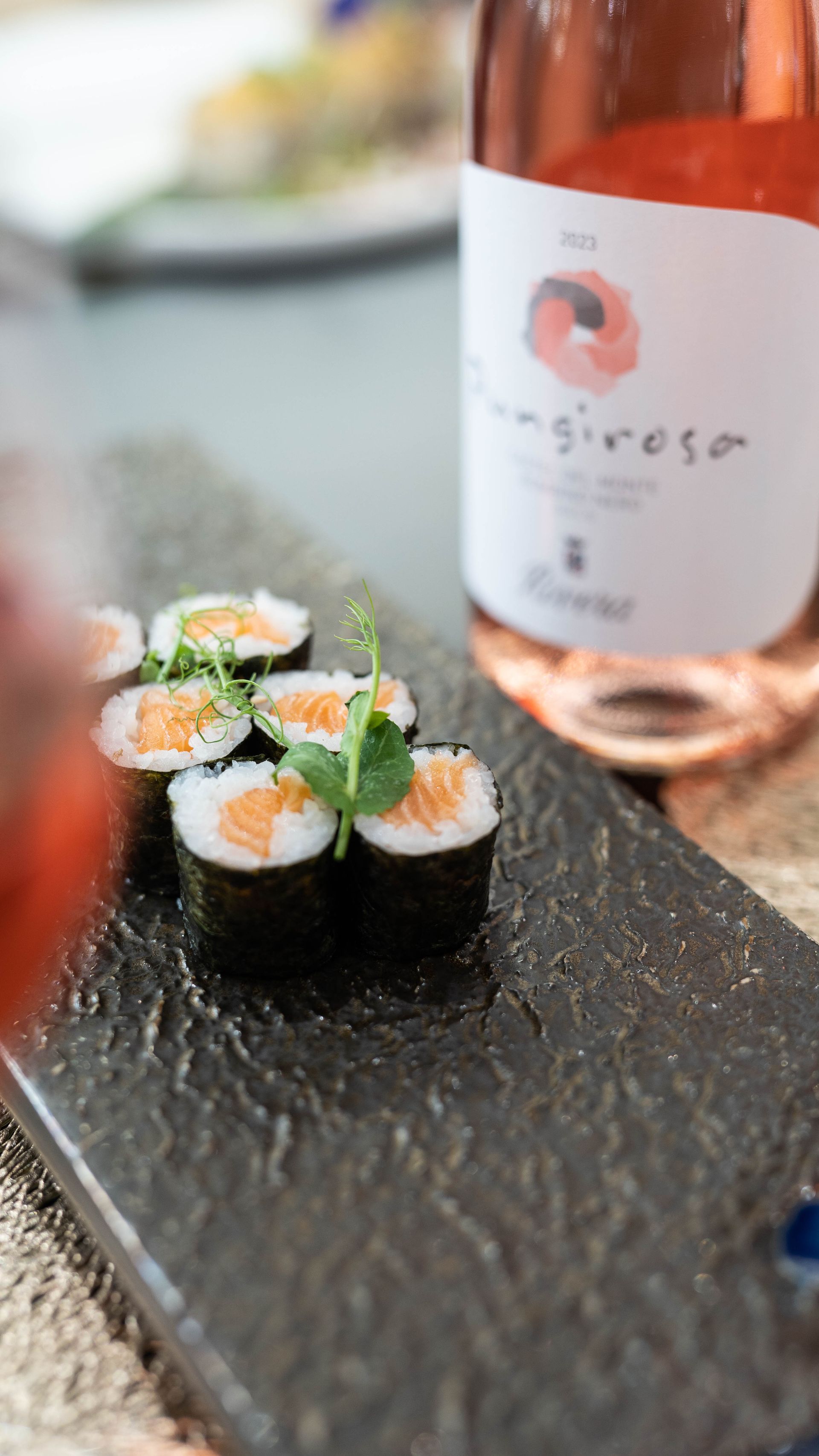 Una bottiglia di vino è seduta accanto a un piatto di sushi.