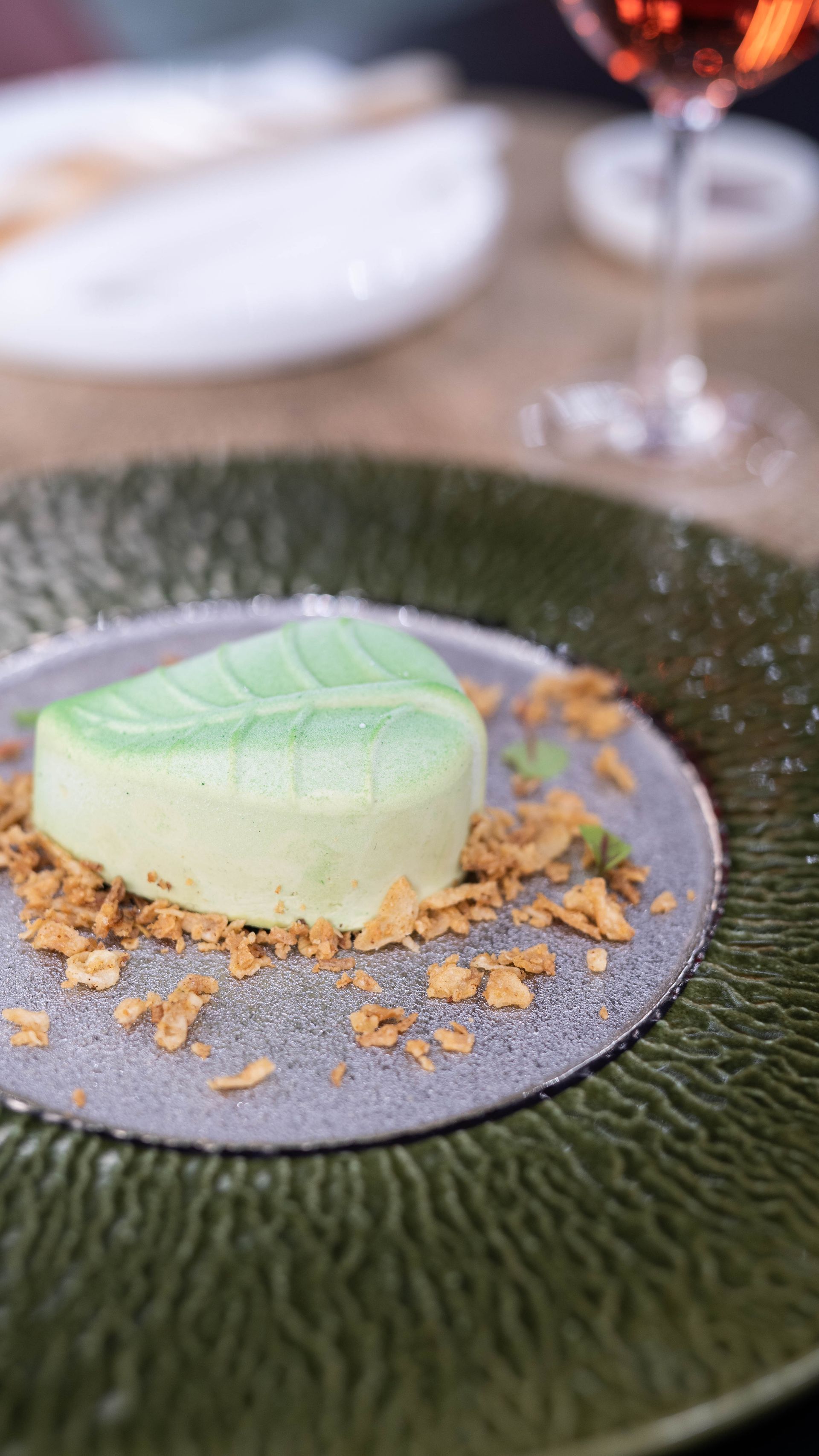 Un primo piano di un dessert su un piatto con un bicchiere di vino sullo sfondo.
