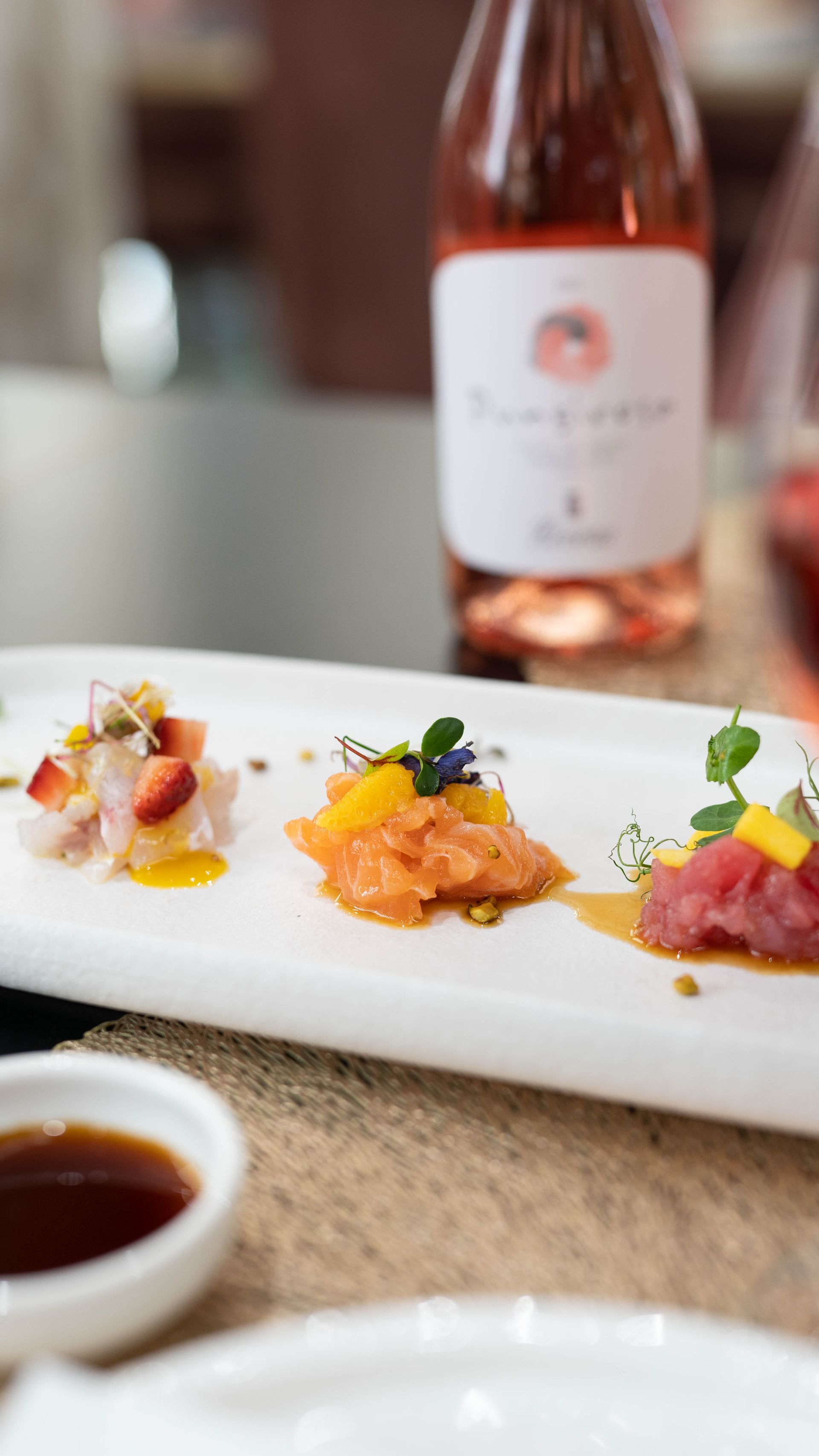Un piatto bianco condito con cibo e una bottiglia di vino su un tavolo.