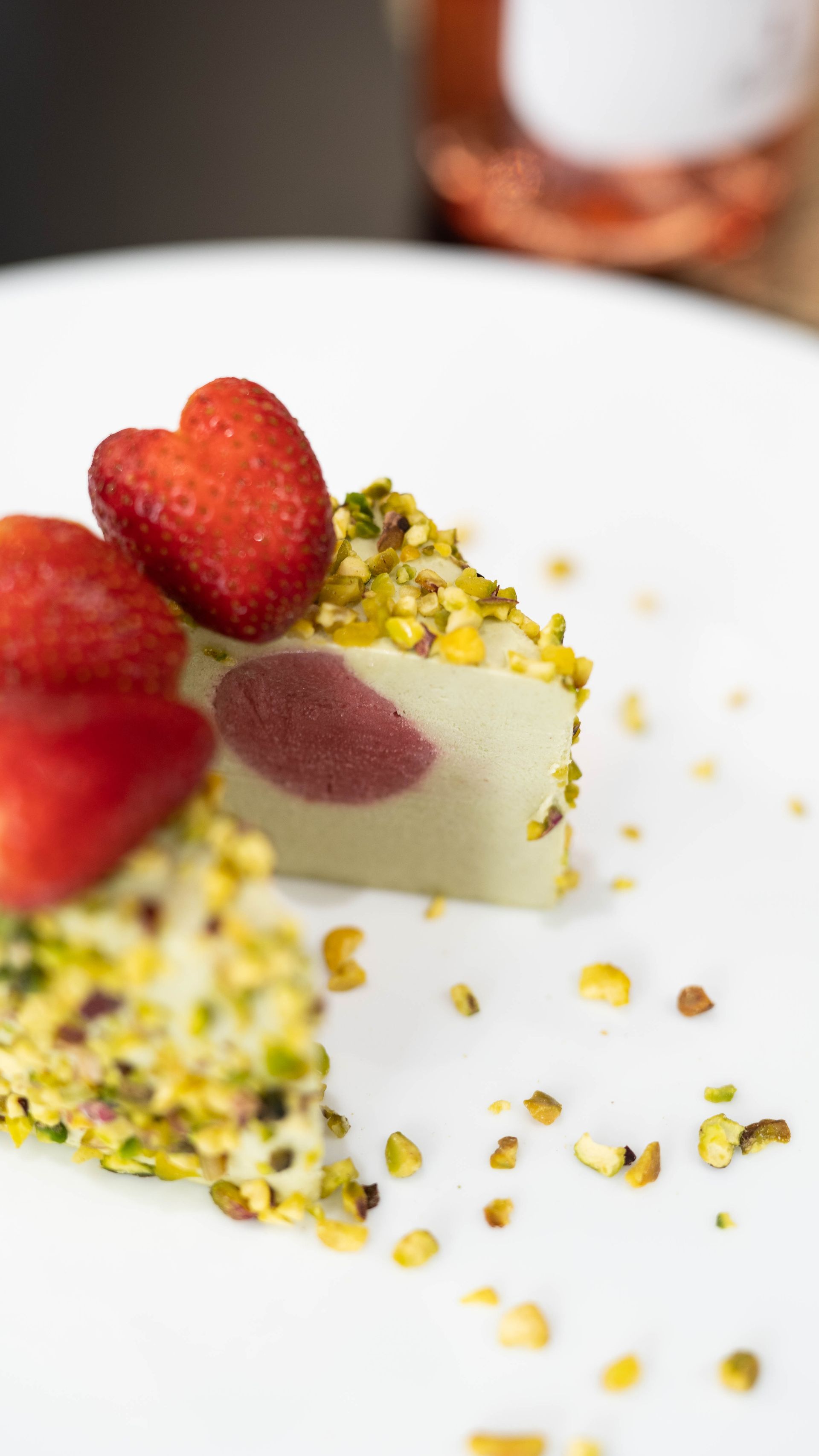 Una fetta di torta con fragole e pistacchi su un piatto bianco.
