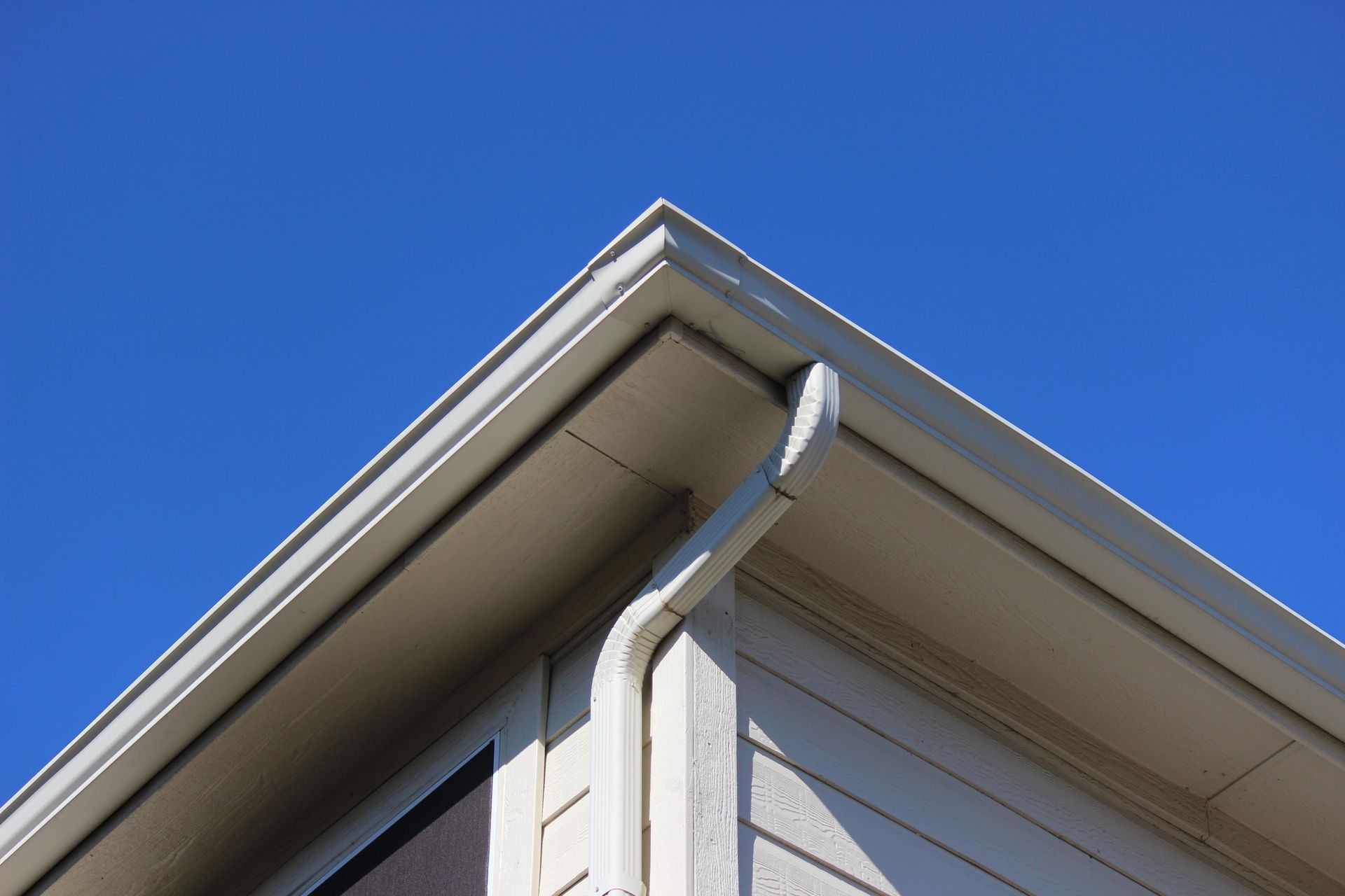Corner of a house with white gutters and downspout against a blue sky.