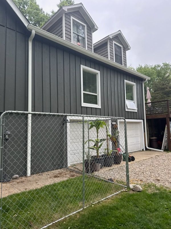 Man in blue shirt and cap cleaning a roof gutter, reaching with gloved hand and pole.