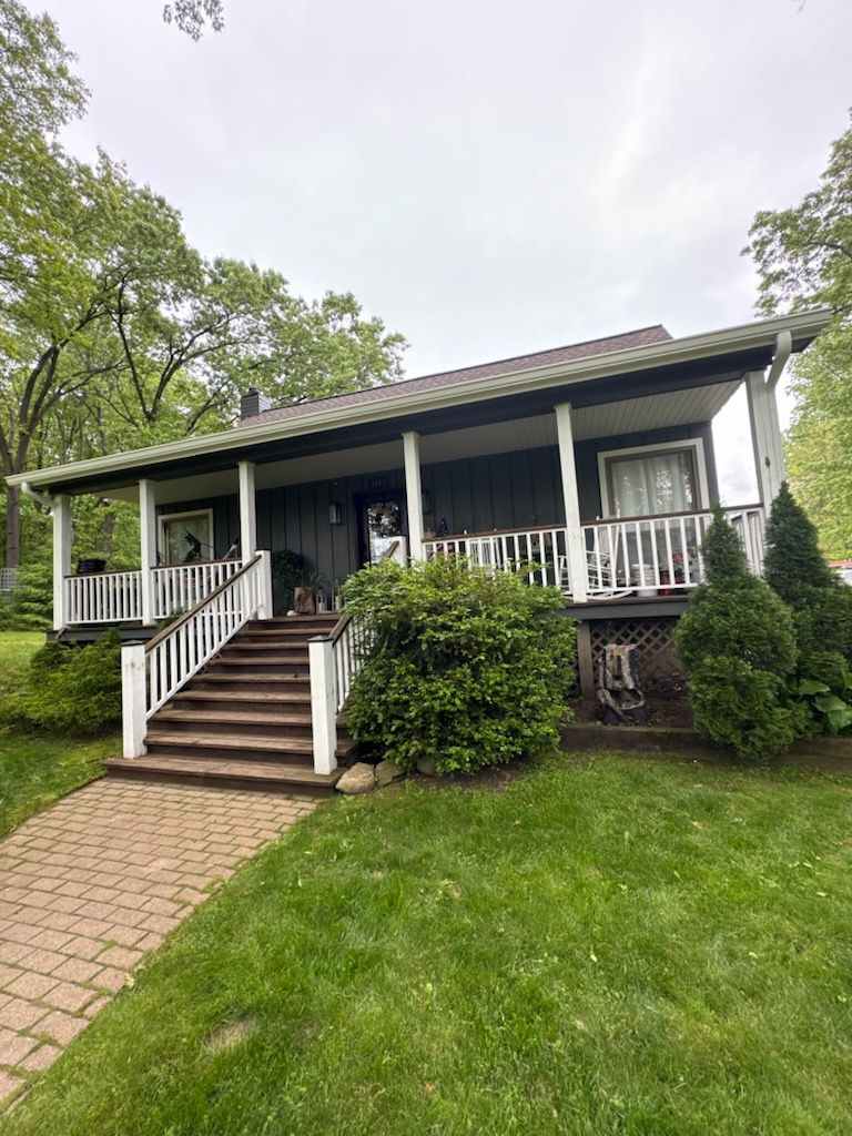 Dark gray house with white porch, brown steps, and brick walkway on a grassy lawn.