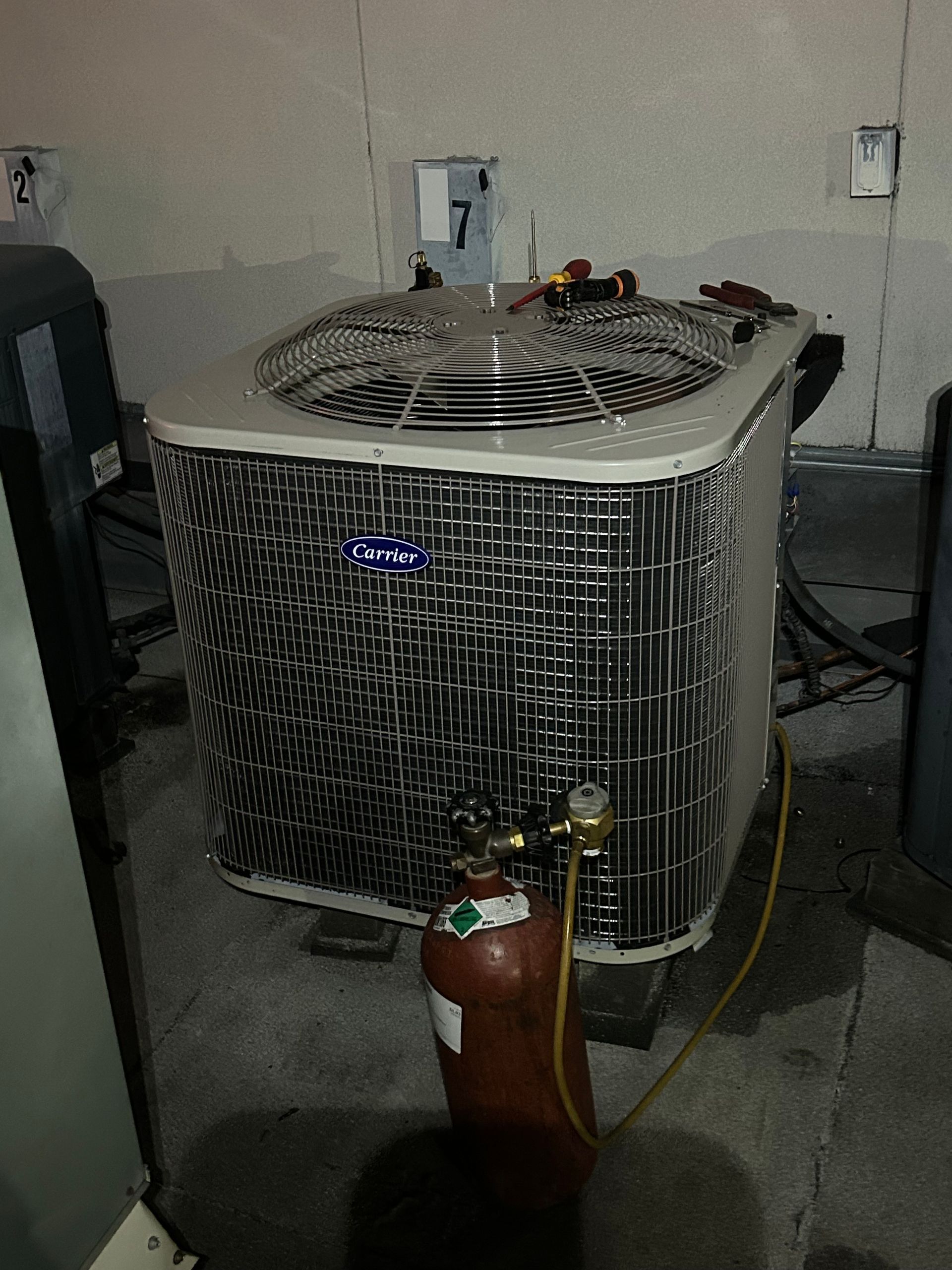 An air conditioning unit with a copper gas tank and hoses in a concrete basement.