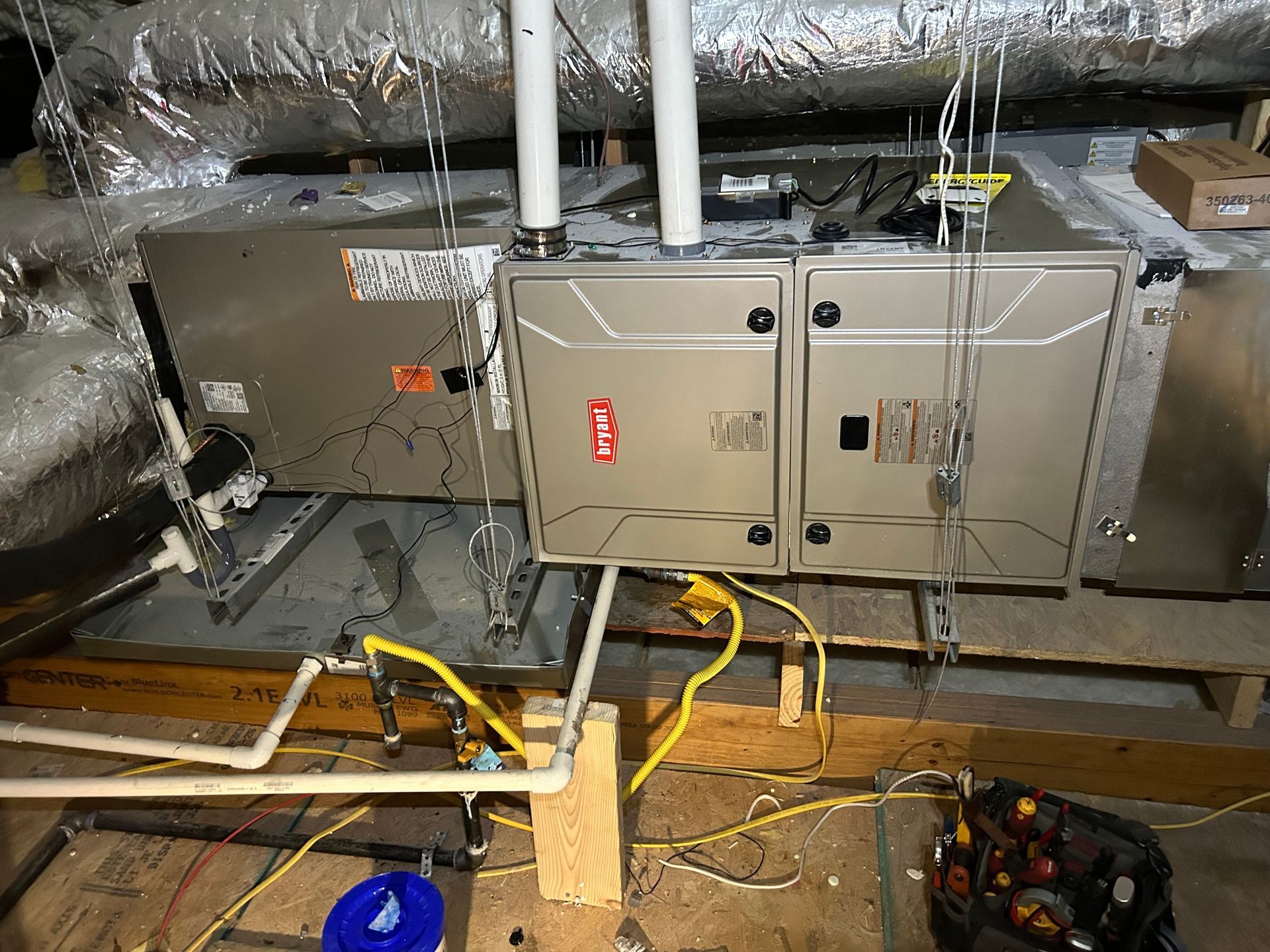 Furnace installation: Silver HVAC units, white pipes, yellow electrical wires, and a black toolbox.