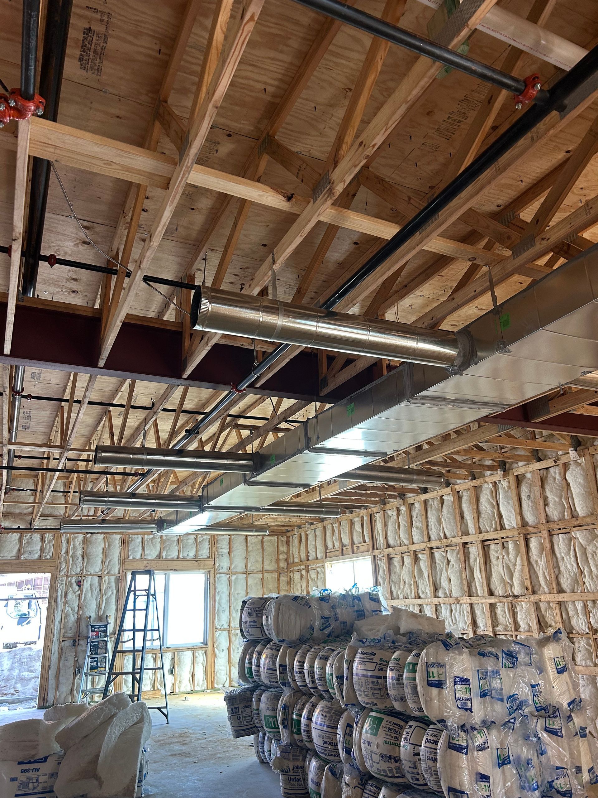 Interior view of a construction site with exposed wooden beams, ductwork, and insulation rolls.