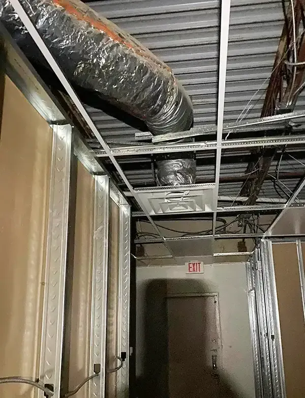 Construction site interior: exposed ceiling with ductwork, metal framing, drywall, and exit sign.