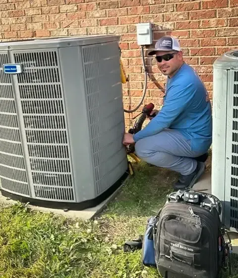 HVAC technician working on an air conditioning unit outside a brick building.