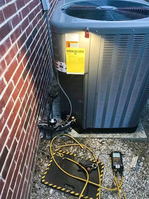 An HVAC unit is being serviced, with gauges and hoses connected. It sits next to a brick wall.