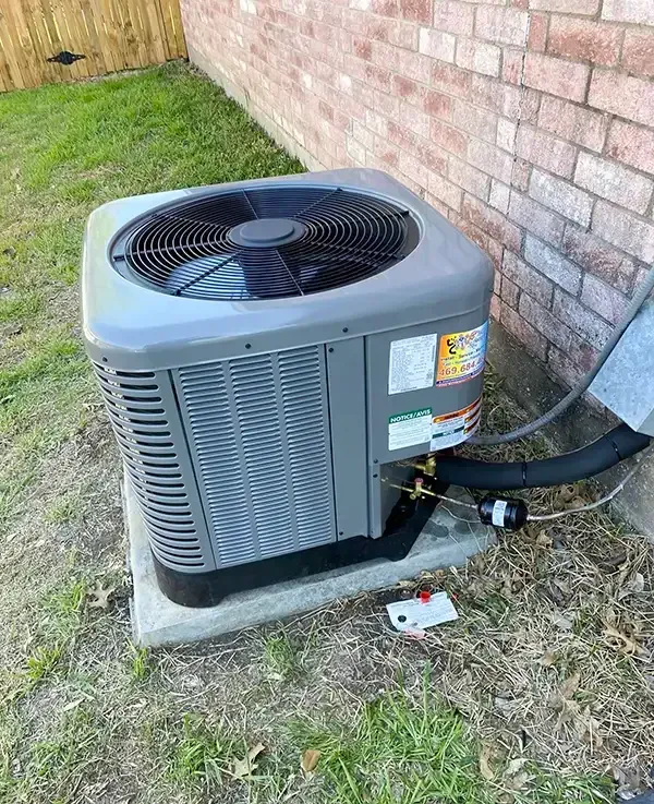 Air conditioning unit on a concrete pad next to a brick wall and grass.