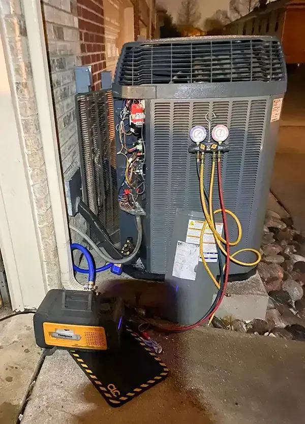 HVAC unit with gauges, hoses, and a vacuum pump. Open side reveals components, setting is outdoors.