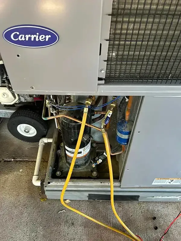 Carrier HVAC unit with yellow hoses connected to a black compressor. Metal casing, gray exterior, visible components.