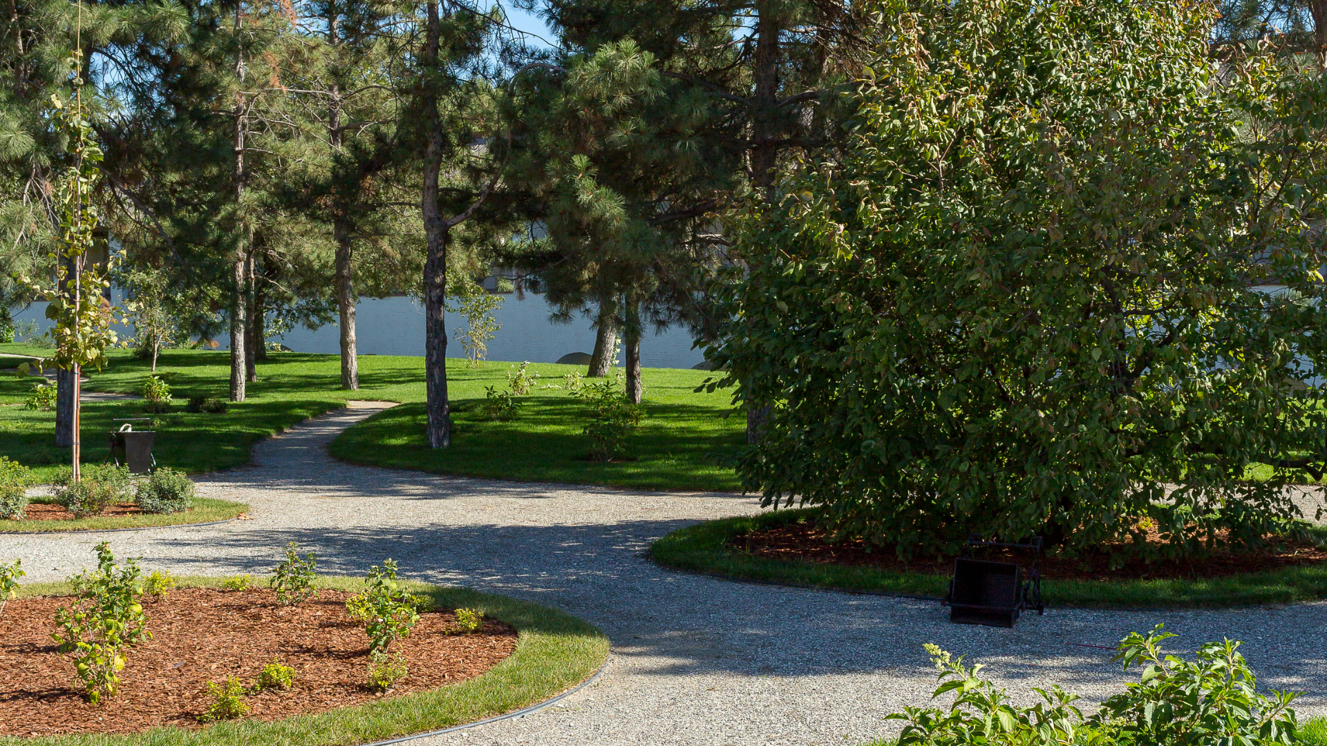 A gravel path in a park with trees and a lake in the background.