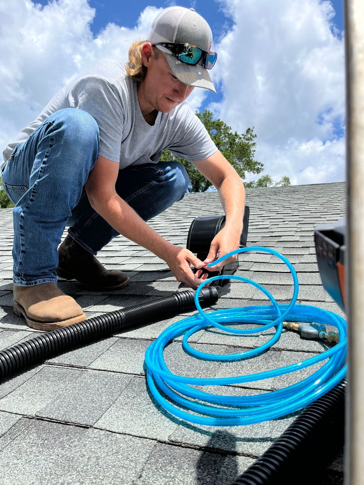 A man is kneeling on a roof next to a blue hose.