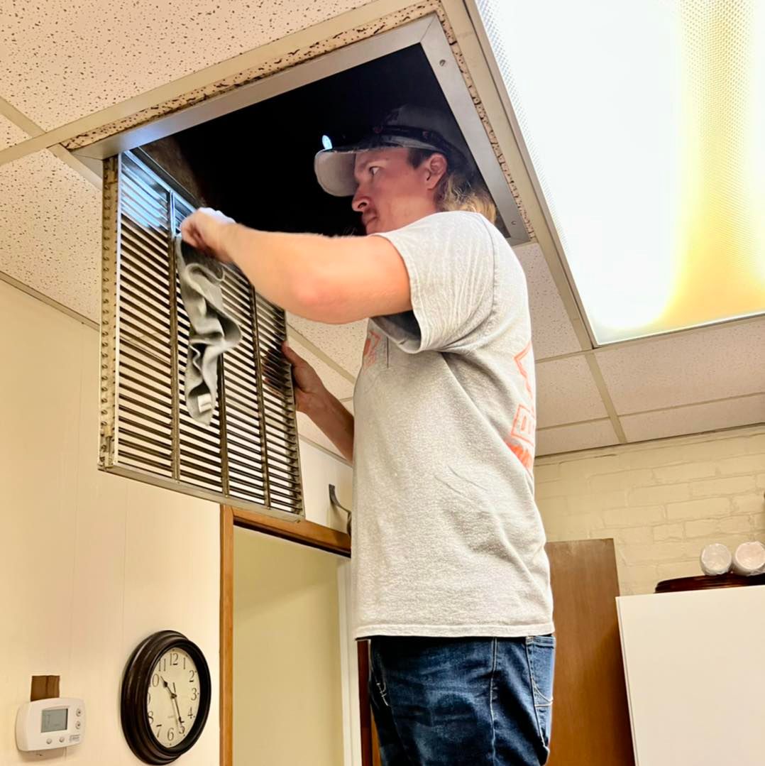 A man in a gray shirt is working on an air vent