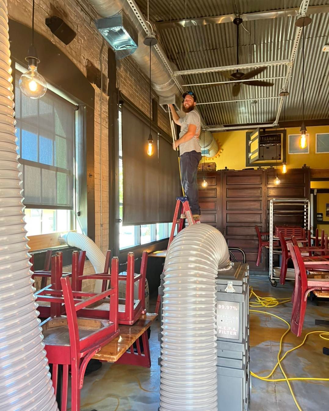 A man is standing on a ladder in a restaurant working on the ceiling.
