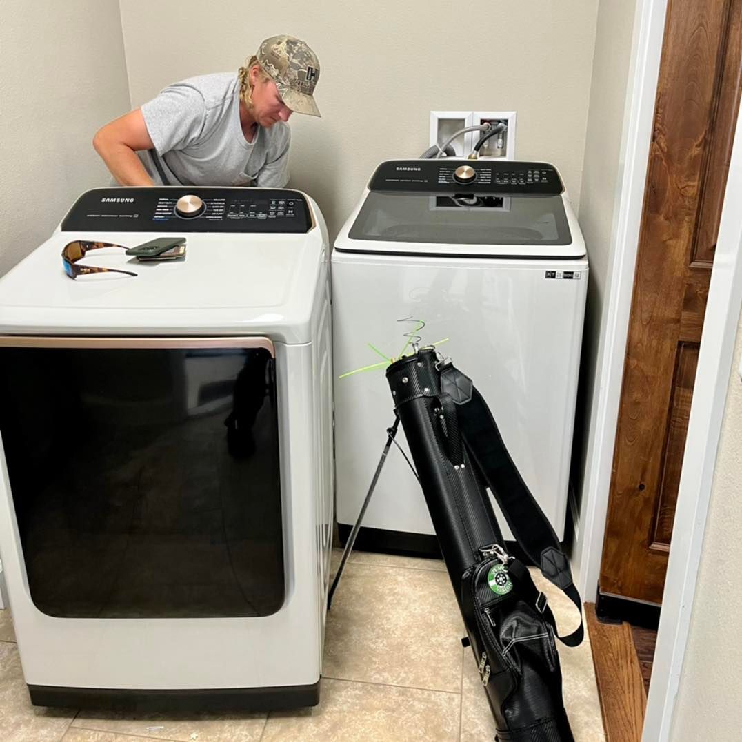 A man is working on a washer and dryer in a laundry room.