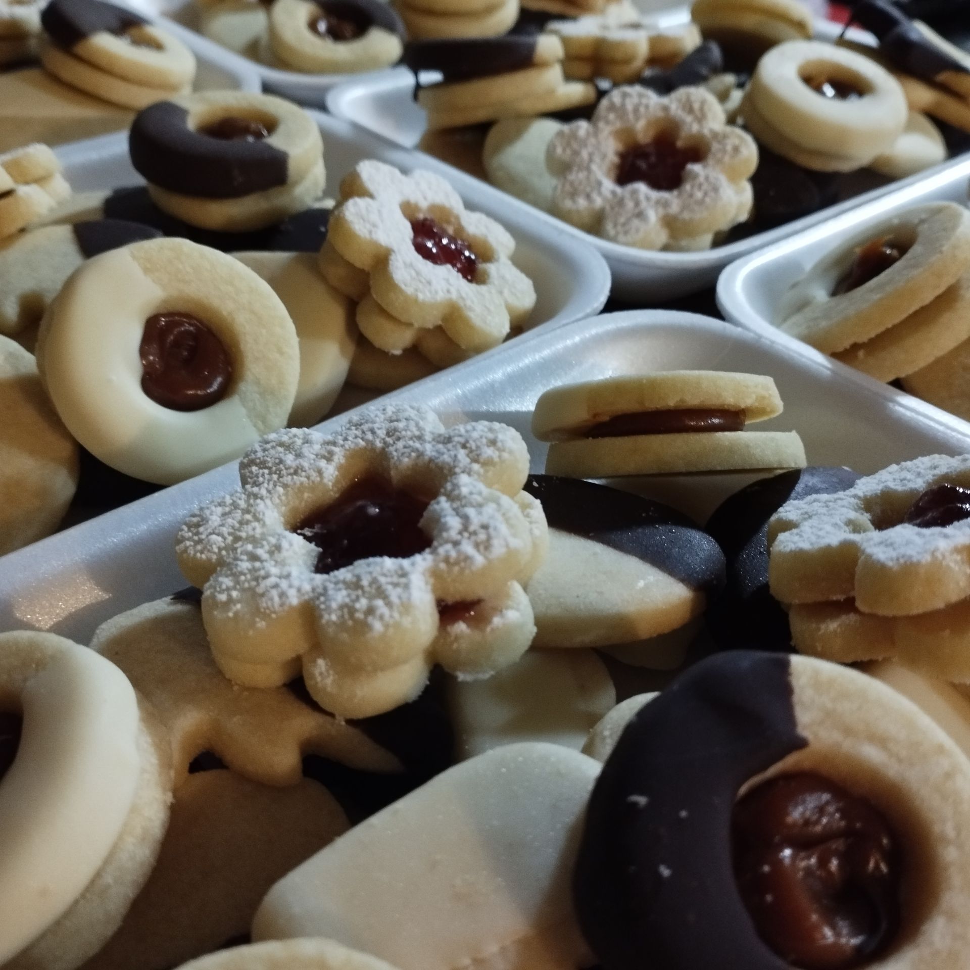 Galletas en una caja: Varias formas, incluidos círculos, cuadrados y flores, dispuestas en filas ordenadas.