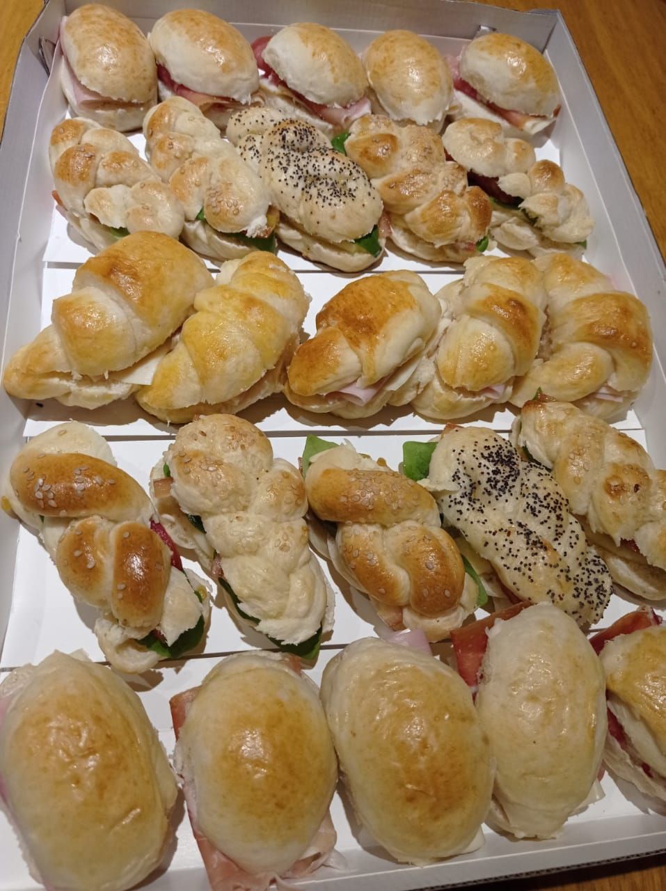 Bandeja de diversos bocadillos pequeños, entre ellos panecillos, croissants y pan trenzado con rellenos.