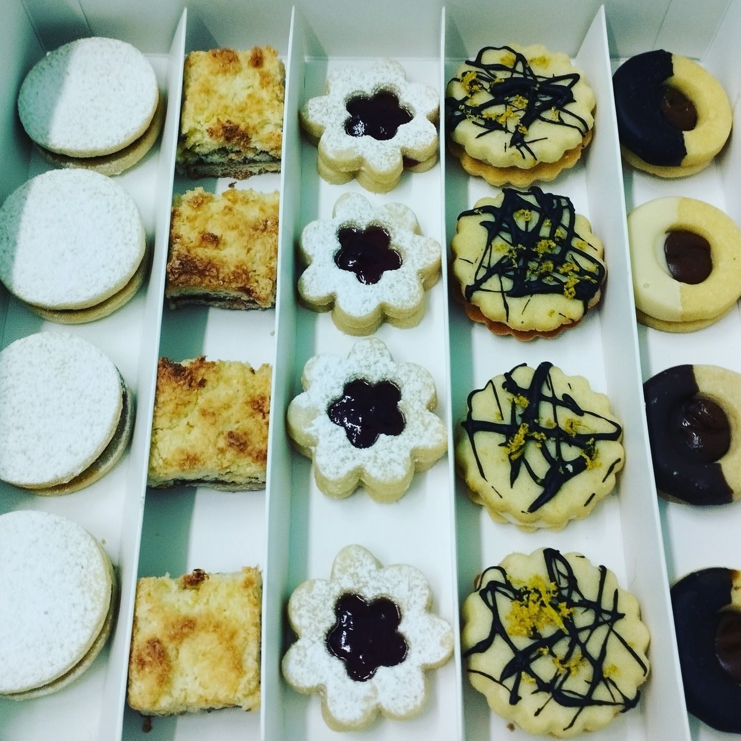 Galletas en una caja: Varias formas, incluidos círculos, cuadrados y flores, dispuestas en filas ordenadas.