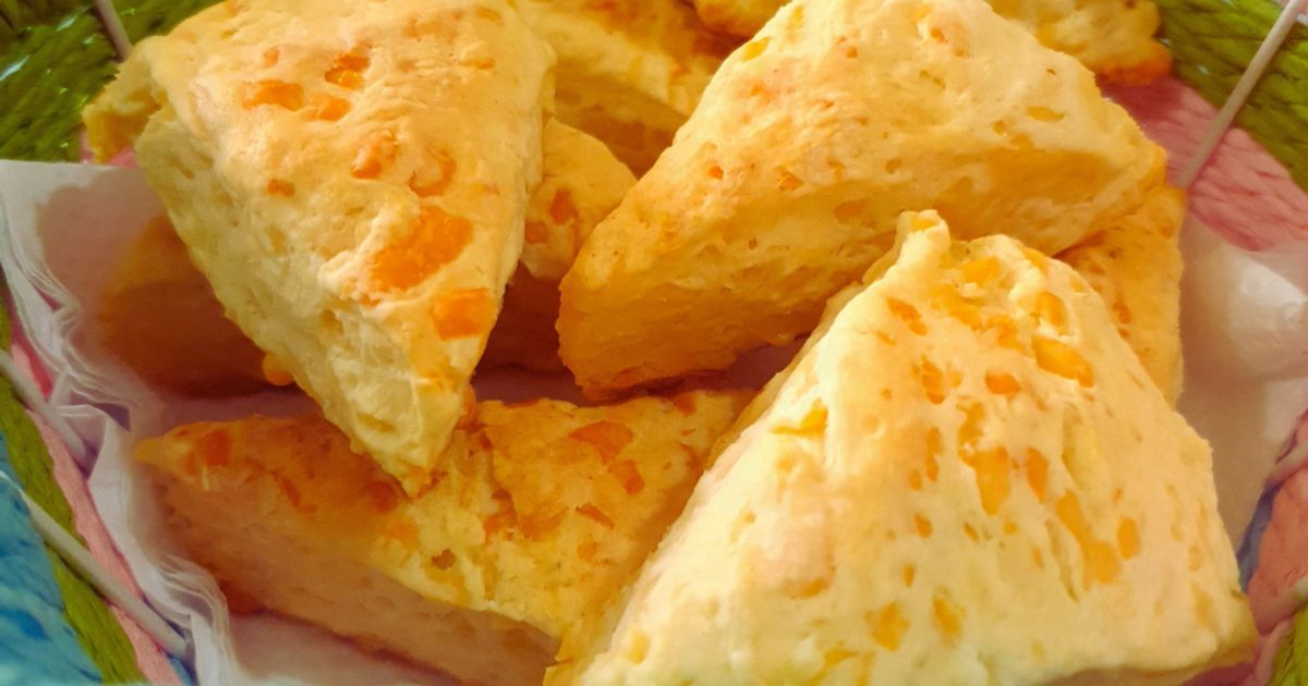 Bollos de queso triangulares en una cesta, con superficies doradas y trocitos de queso naranja.